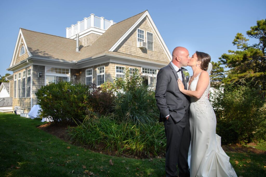 Beautiful Cape Cod wedding set against the backdrop of a quintessential beach cottage as the couple shares a kiss.

