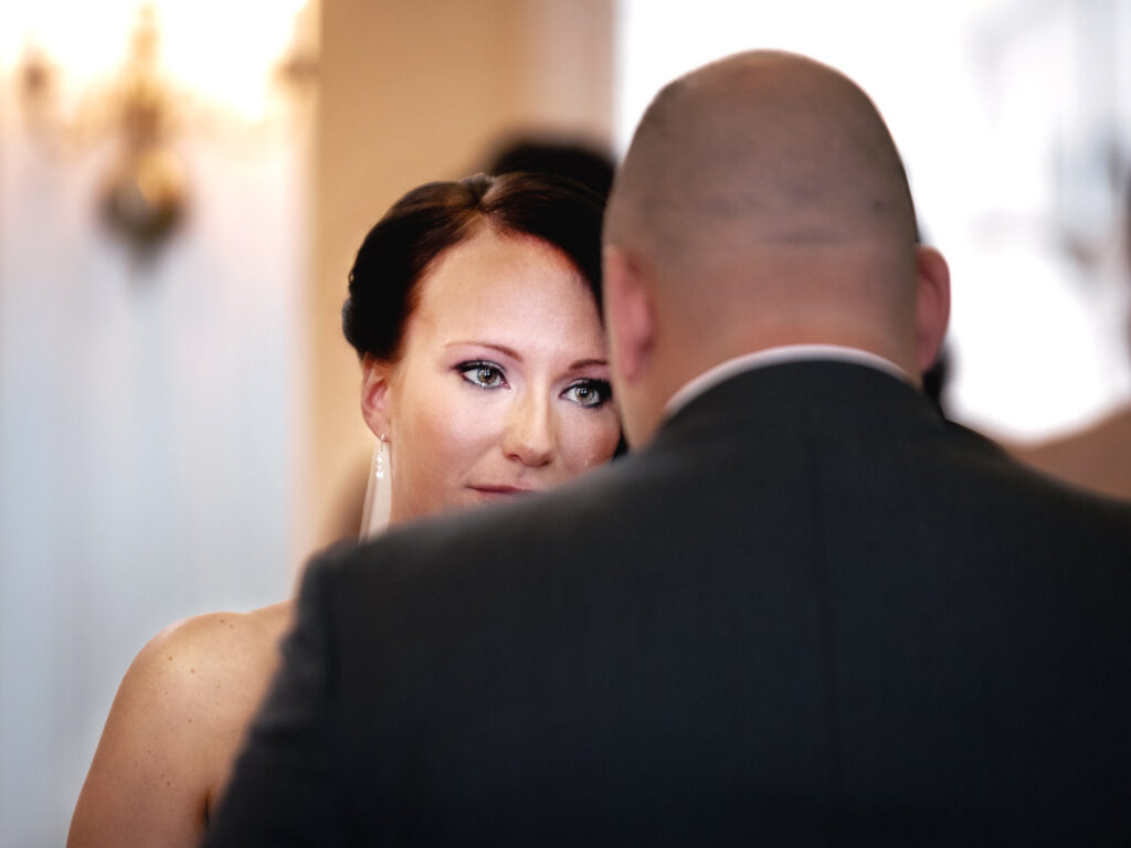 Intimate moment captured between a bride and groom, with the focus on the bride's expressive eyes as she gazes past the groom's shoulder, hinting at a heartfelt exchange