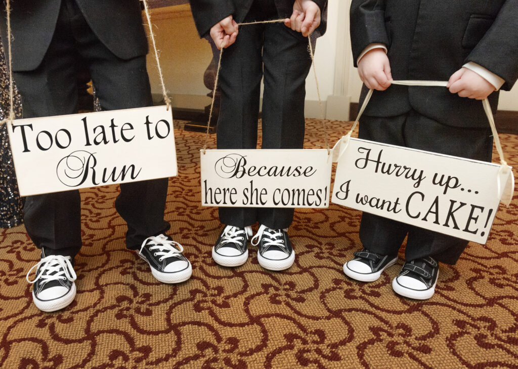 Close up view of three young boys wearing converse sneakers and holding signs that read "too late to run" "because here she comes" and "hurry up...I want cake"