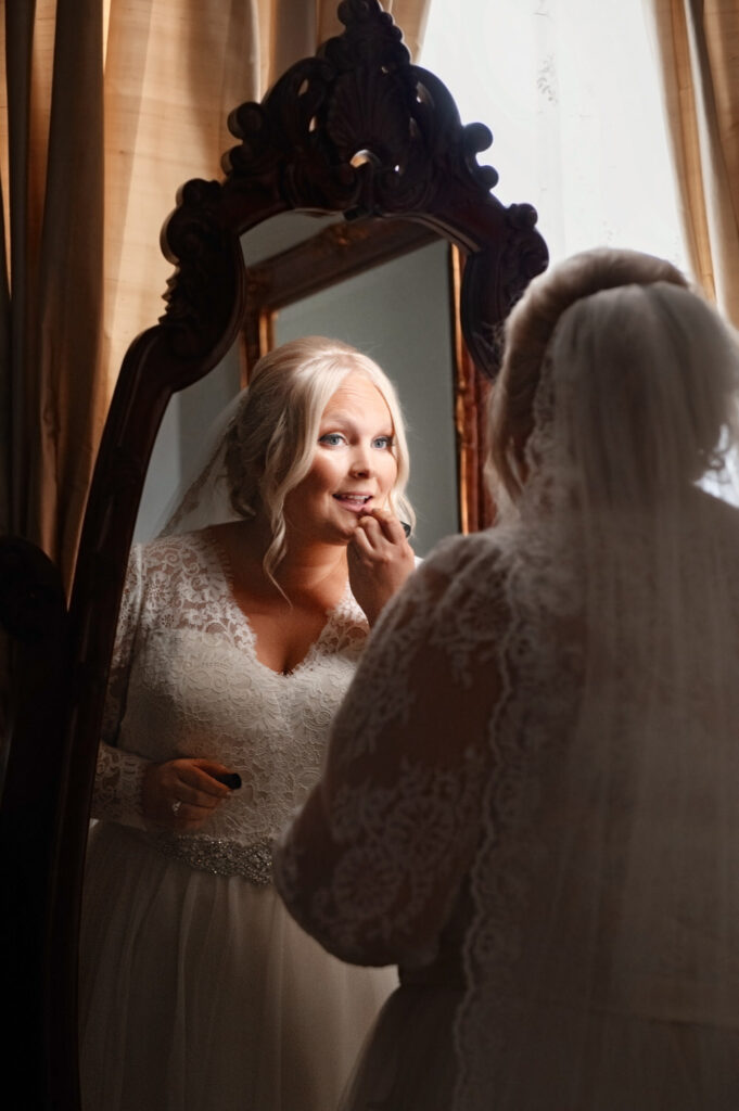 Rear view photo of bride putting her lipstick on in antique mirror