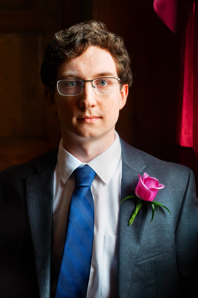 Closeup shot of groom with blue tie and pink rose pinned to his lapel
