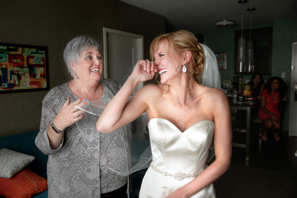 A joyful bride shares a laugh with an older woman, both expressing genuine happiness and excitement on the wedding day