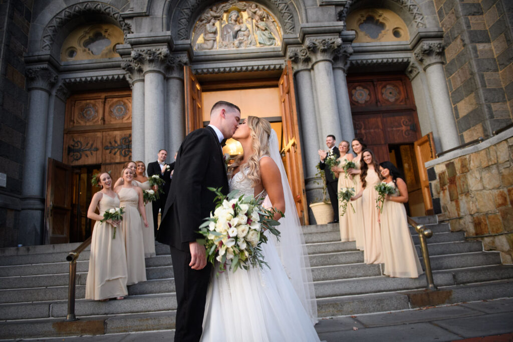 Bride and groom share a kiss in front of the Hyatt Regency steps with bridesmaids in light colored dresses standing on either side of them
