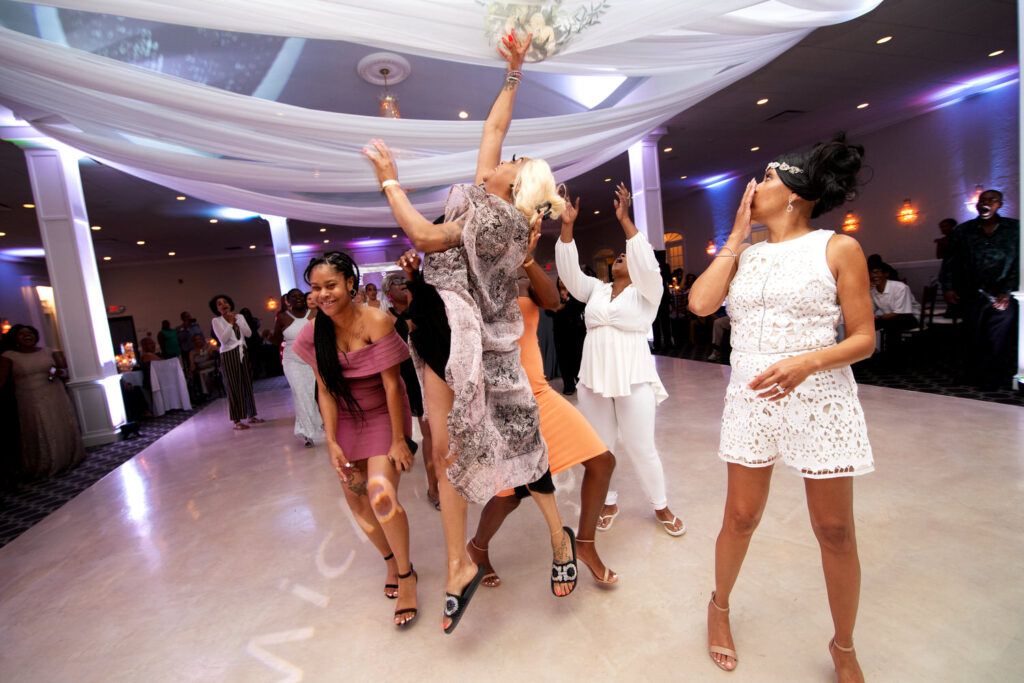 Excited guests jump to catching wedding bouquet on dance floor with other guests surrounding the dance floor