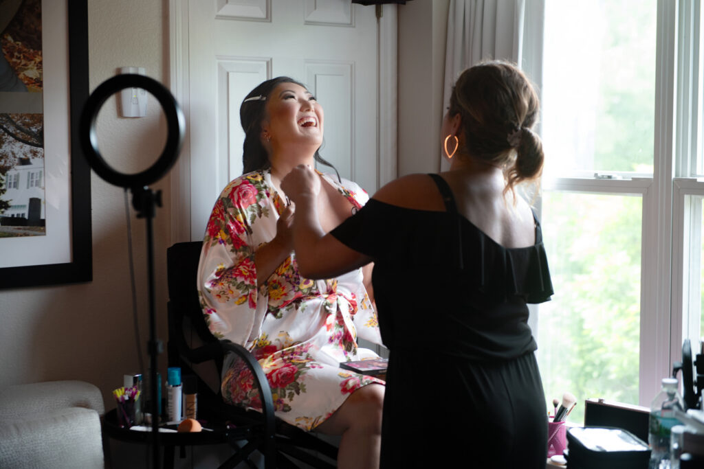 Bride shares a laugh while getting make up done for her wedding in a floral robe