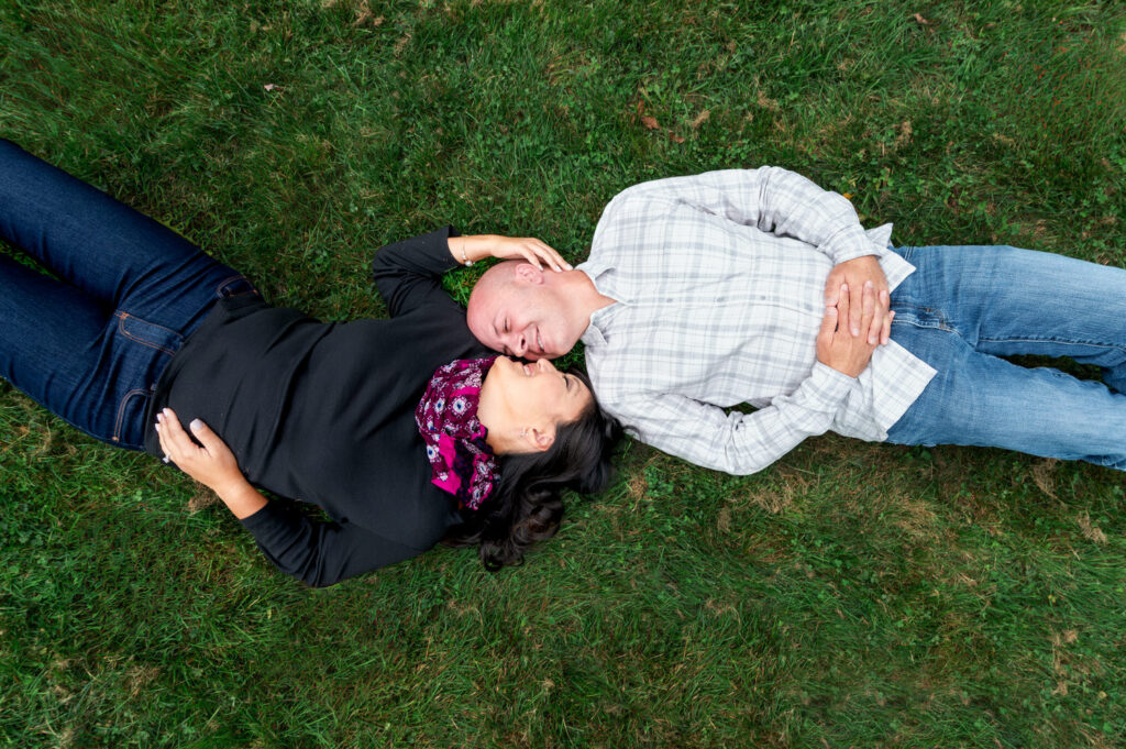 GPT
A couple is lying down on a grassy lawn, viewed from above. The woman, in a black top and blue jeans, is on her left side facing the man, who wears a plaid shirt and jeans. They hold a relaxed pose, suggesting a moment of comfortable intimacy in a peaceful outdoor setting, likely in a park or garden.