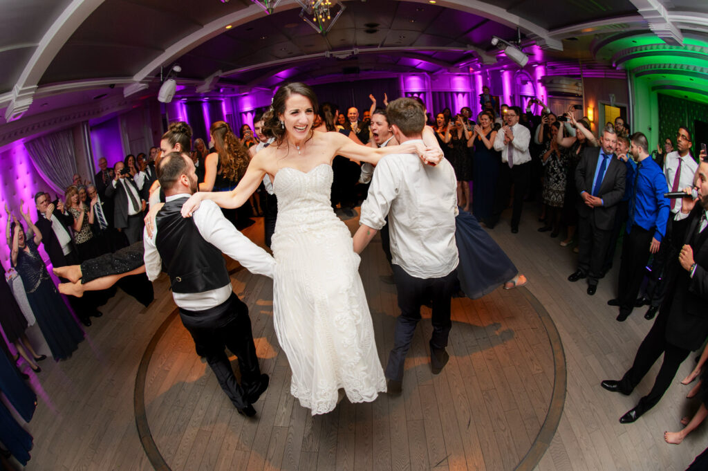 Fish eye view of bride on dance floor surrounded by guests with purple and green lights in the background