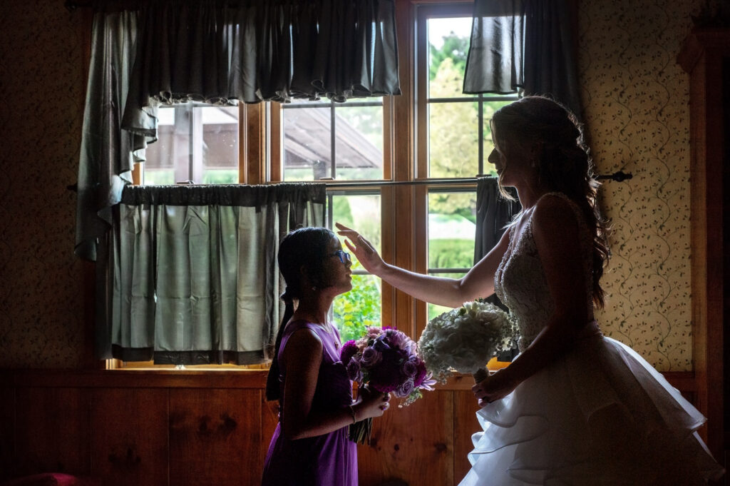 Shadowed shot of bride holding bouquet while sharing a tender moment with flower girl in purple dress