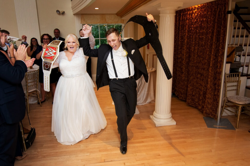 Bride and groom celebrating in reception hall while holding wrestling belts