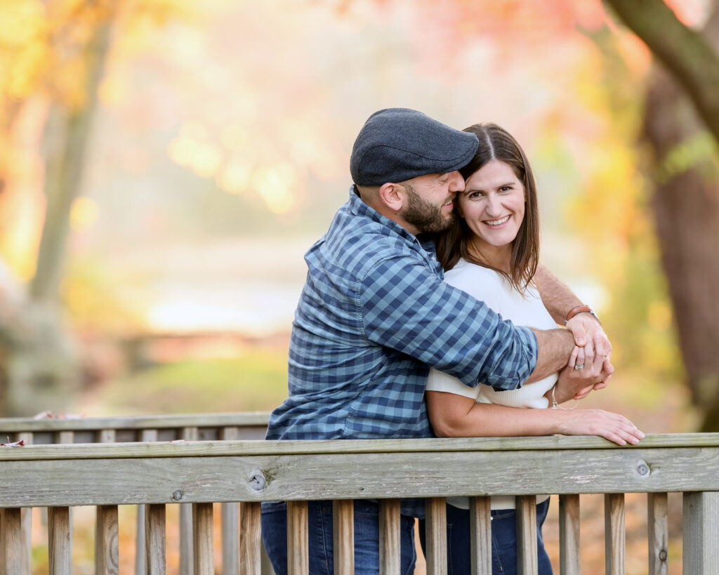 A couple poses while hugging one another outdoors in fall.