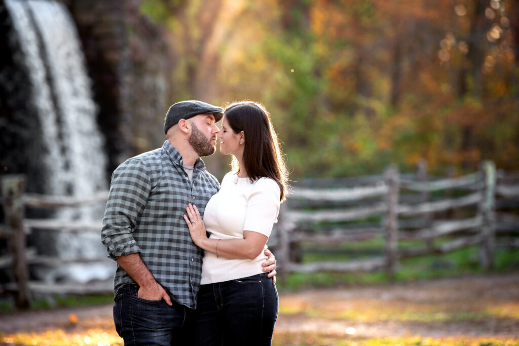 A couple leans in for a kiss by a waterfall.