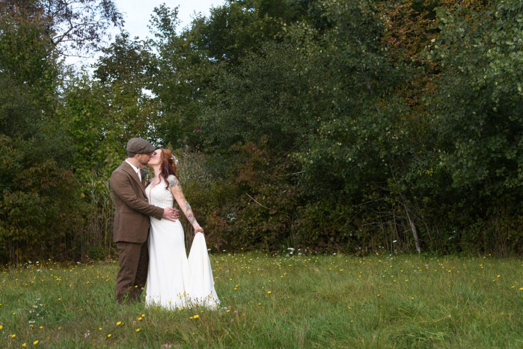A newlywed couple kissing in a field. 