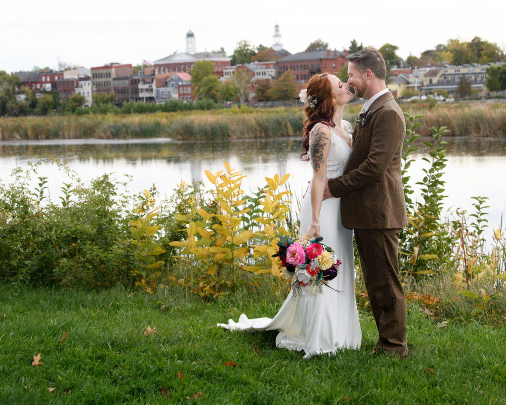 A newlywed couple kissing in front of a small lake. 