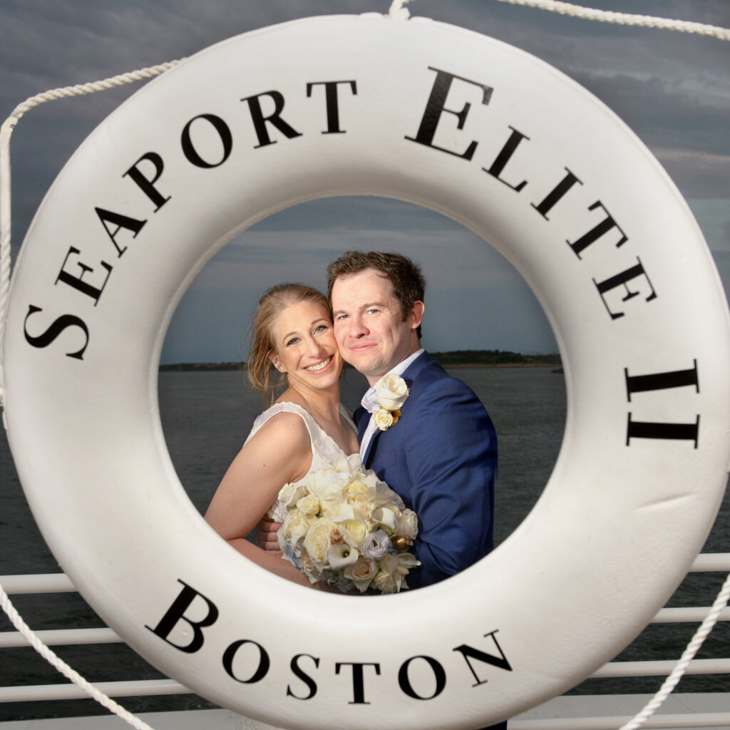 The same couple framed through a life preserver reading "Seaport Elite II Boston," smiling as they hold each other, with the harbor visible in the background.