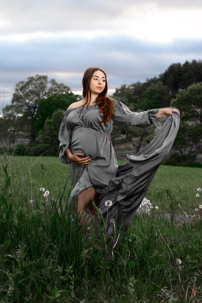 A woman holding out the back of her dress with one hand and bottom of her pregnant stomach with the other 