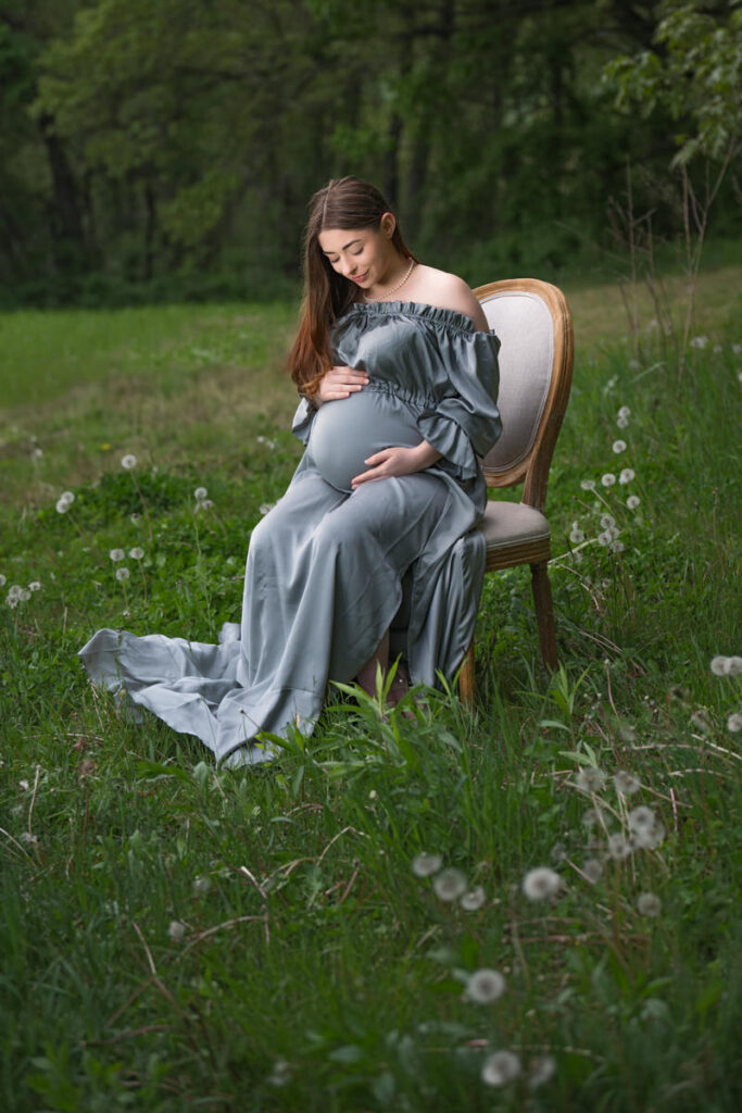 A pregnant woman sitting in a chair in a field looking down at her stomach 