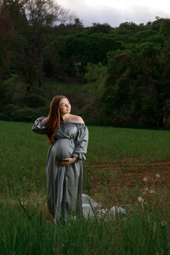 A woman adjusting her hair with one hand and holding her pregnant stomach with the other 