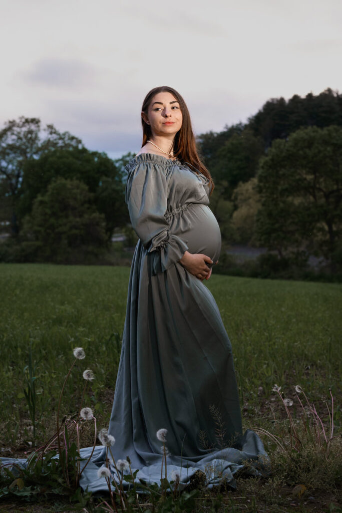 A pregnant woman with a slight smile holding her stomach 