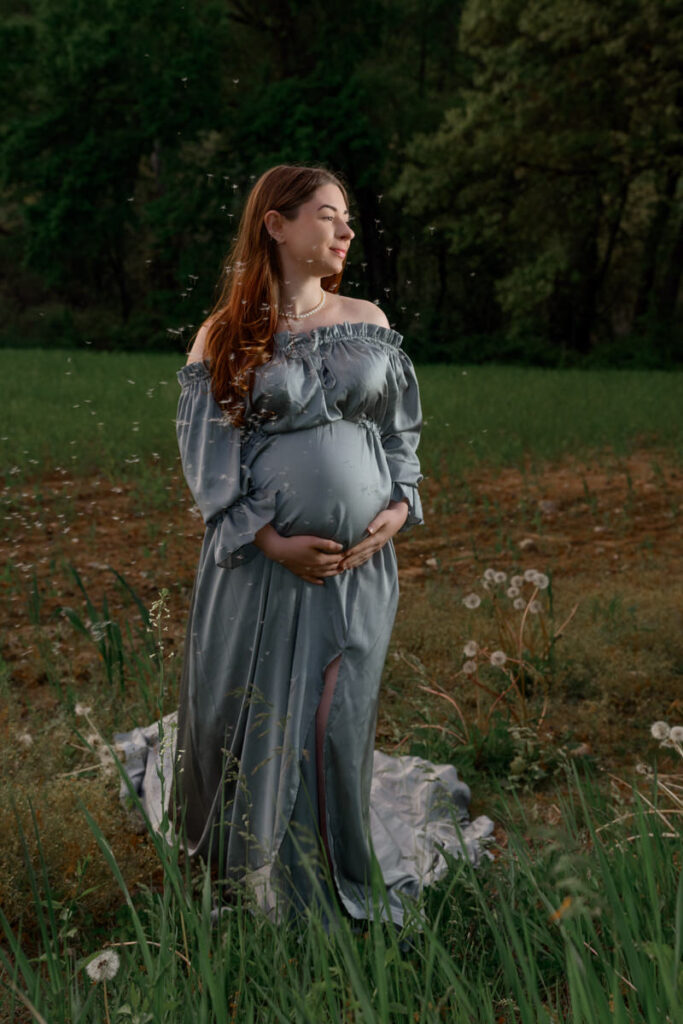 A pregnant woman in a field looking off to the side and holding her stomach 