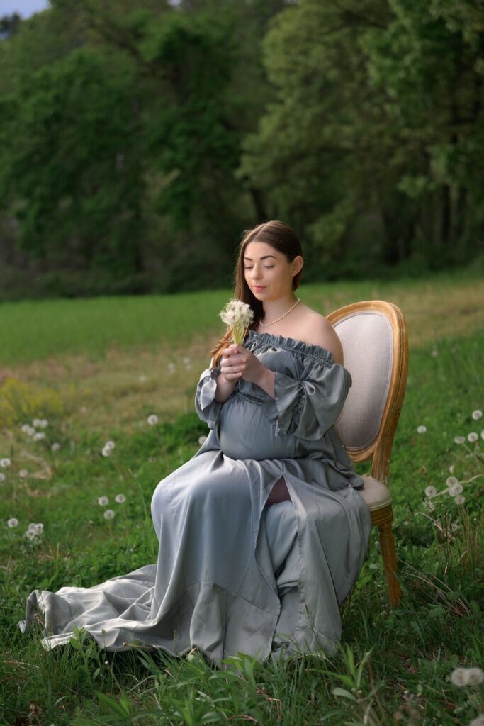 A pregnant woman sitting in a chair in a field holding a flower