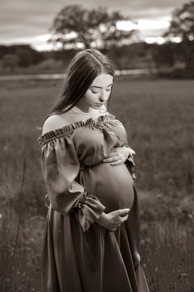 Black and white photo of a pregnant woman holding her stomach and looking down 