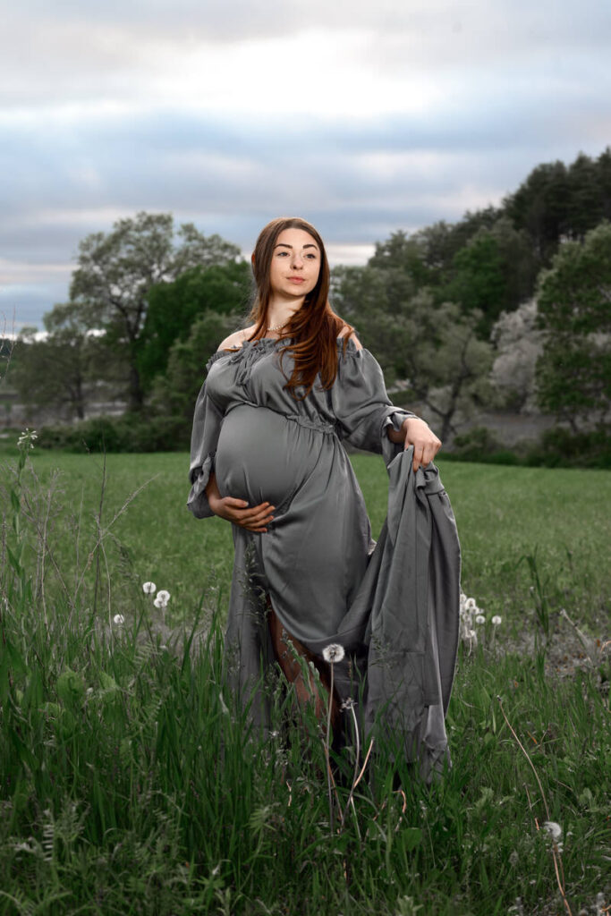 A pregnant woman holding her stomach with one hand and her dress with the other 